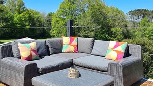 Um sofá modular cinza com almofadas coloridas sobre um deck de madeira, cercado por vegetação.