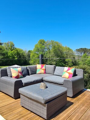 A gray sectional sofa with colorful cushions on a wooden deck, surrounded by greenery. - The Stables - One Bedroom (Cassagnes)