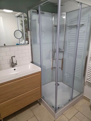 Un baño moderno con ducha envuelta en vidrio, lavamanos blanco y tocador de madera.