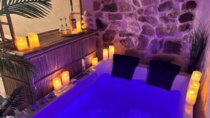 Un espacio de spa con pared de piedra, velas y una bañera.