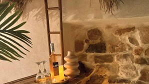 Zona de spa con pared de piedra, bañera, velas y bandeja con una botella y copas.