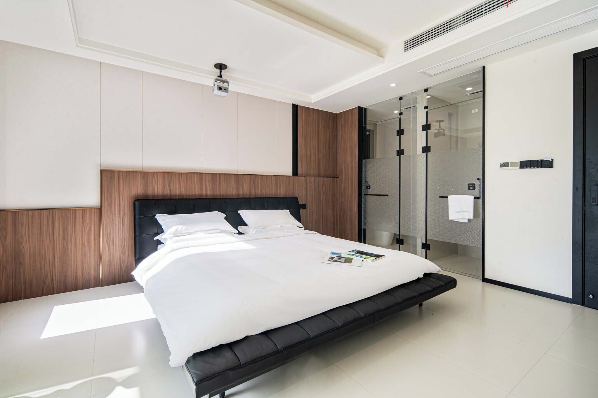 Ein modernes Hotelzimmer mit einem großen Bett, einer Duschkabine aus Glas und einem klaren, minimalistischen Design.
