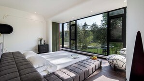 Ein modernes Schlafzimmer mit großem Fenster, einem Bett, einer Bank und einem Fernseher.