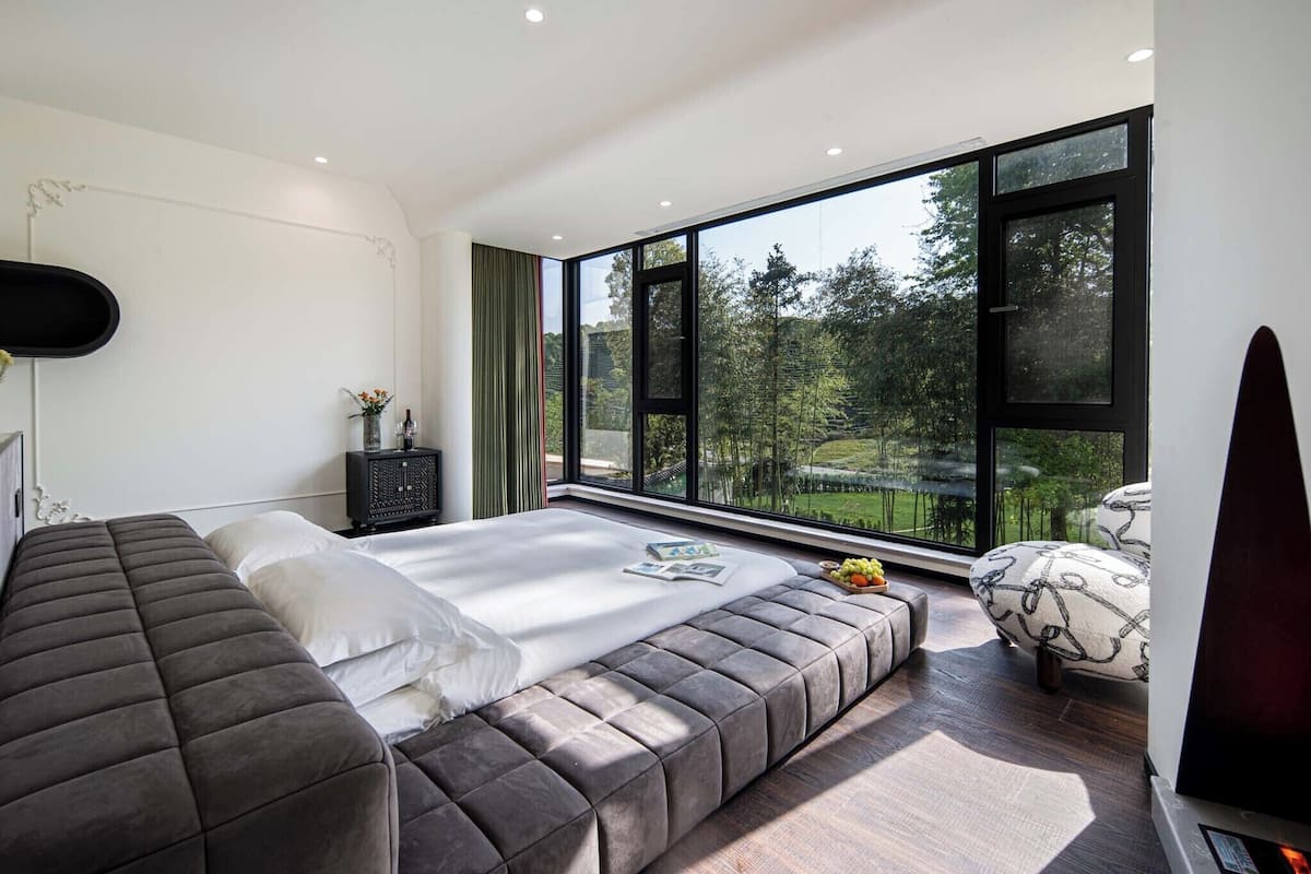 Une chambre moderne avec une grande fenêtre, un lit, un banc et un téléviseur.