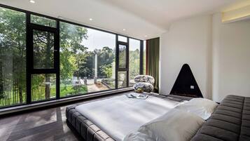 A modern bedroom with a large window, a bed, a seating area, and a fireplace.