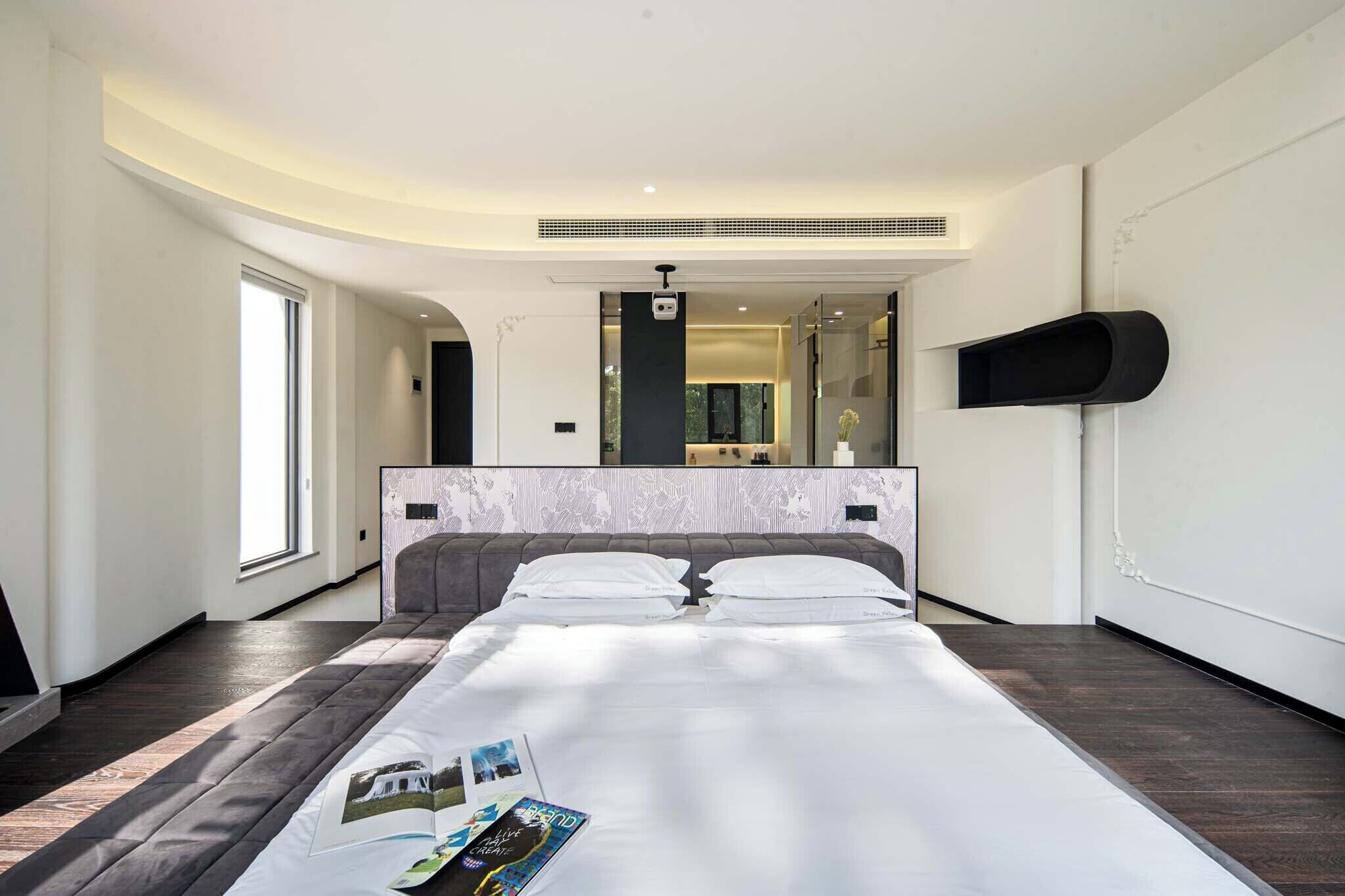 A modern hotel room with a large bed, a built-in TV, a mirror, and a small shelf.