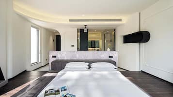 A modern hotel room with a large bed, a built-in TV, a mirror, and a small shelf.