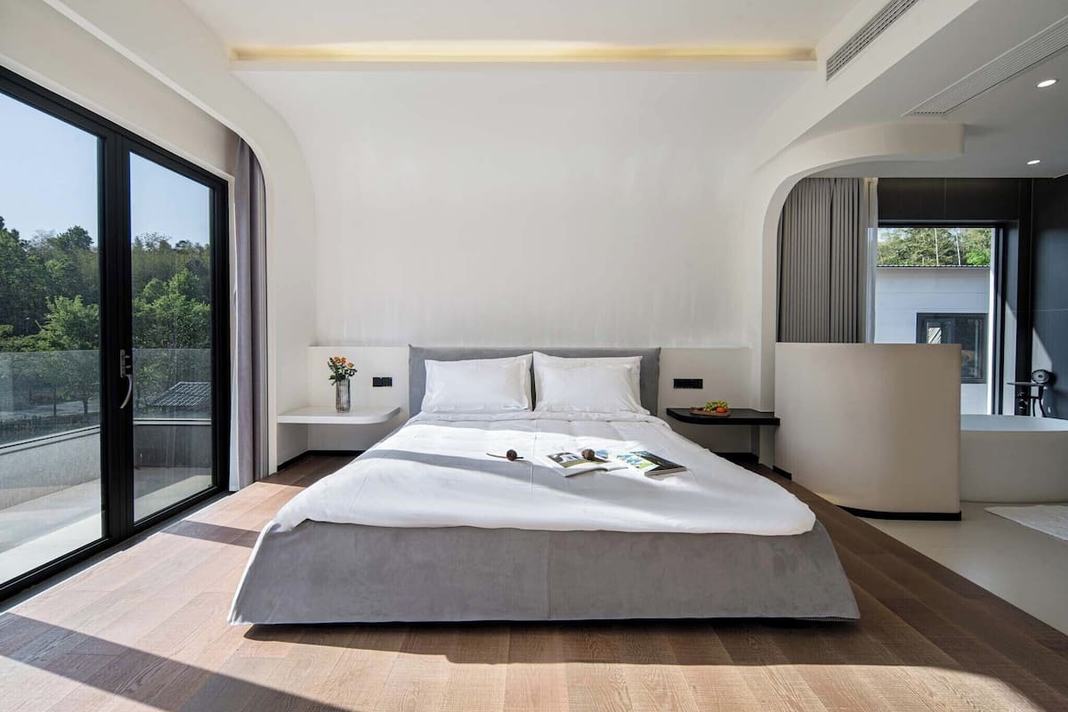 Une chambre moderne avec un grand lit, des tables de chevet, une vue à travers une porte coulissante et un banc intégré.