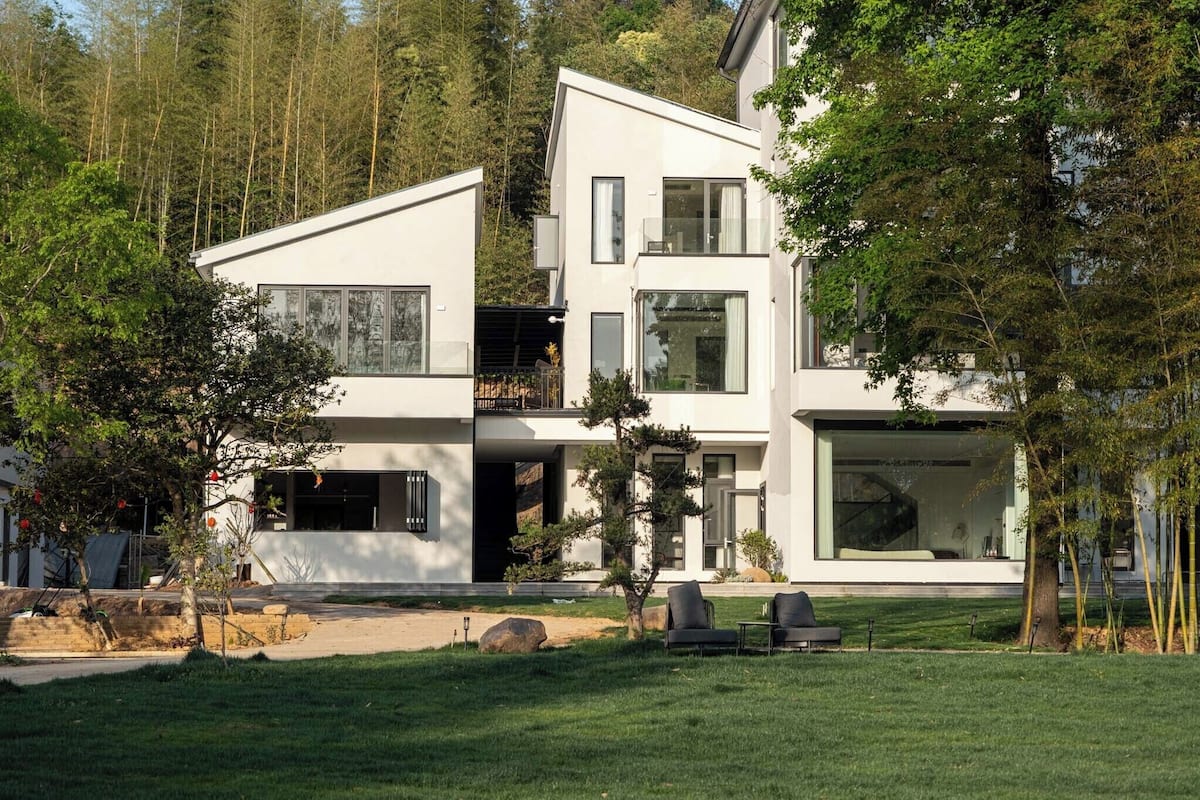 Une maison moderne à deux étages, dotée de grandes fenêtres, d’un balcon et d’une pelouse bien entretenue.