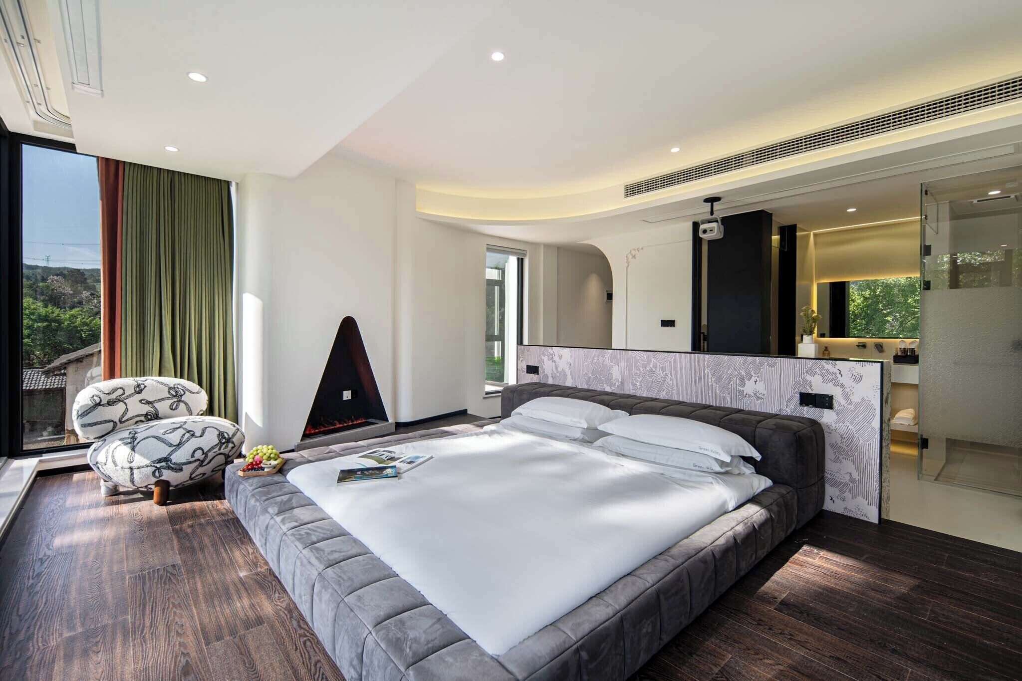 A modern bedroom with a large bed, a sofa, a TV, and a bathroom visible through an open door.