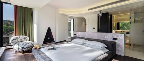 A modern bedroom with a large bed, a sofa, a TV, and a bathroom visible through an open door.