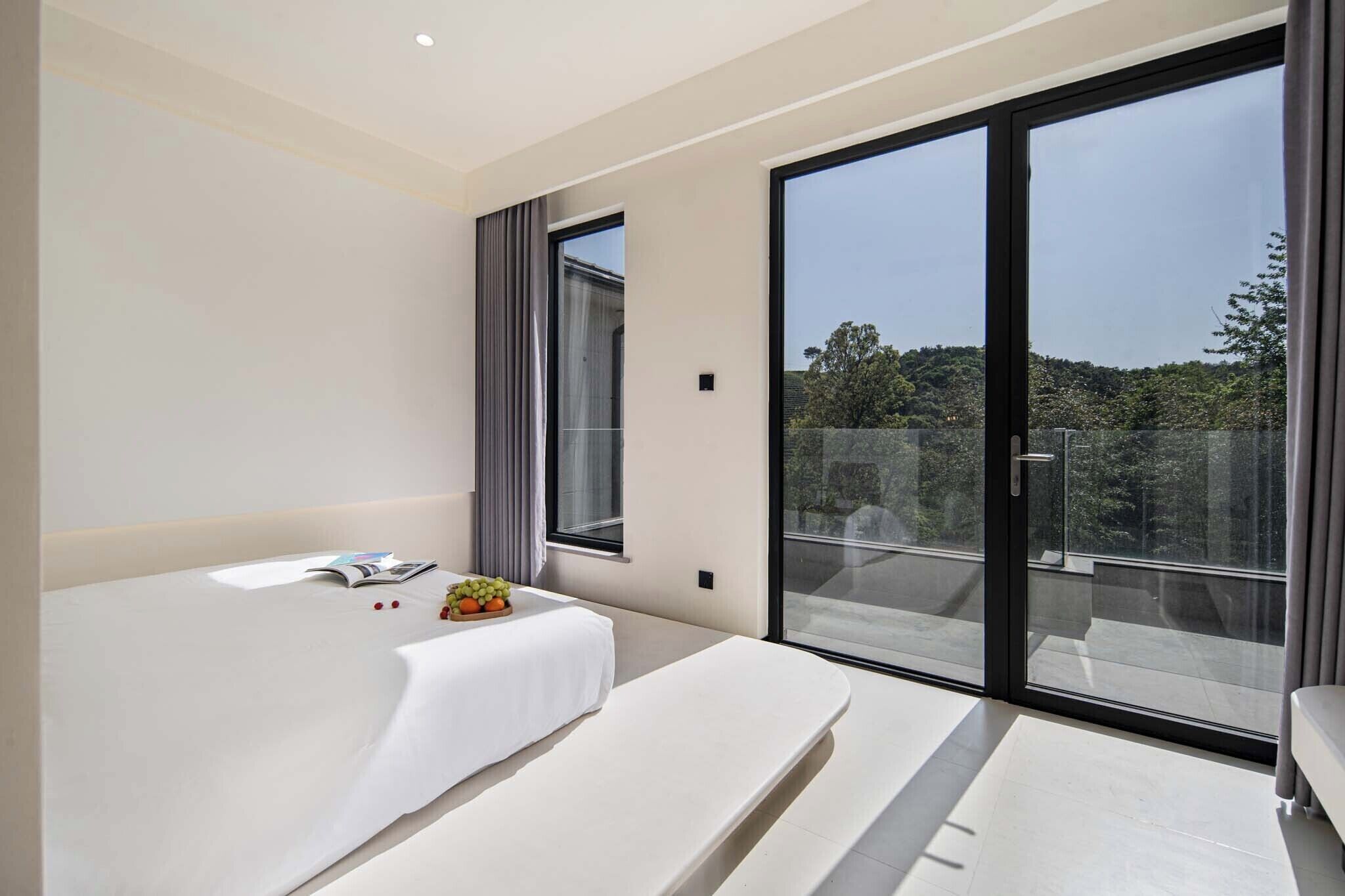 A modern bedroom with a large bed, a bedside table with a fruit bowl, and a sliding glass door leading to an outdoor area.