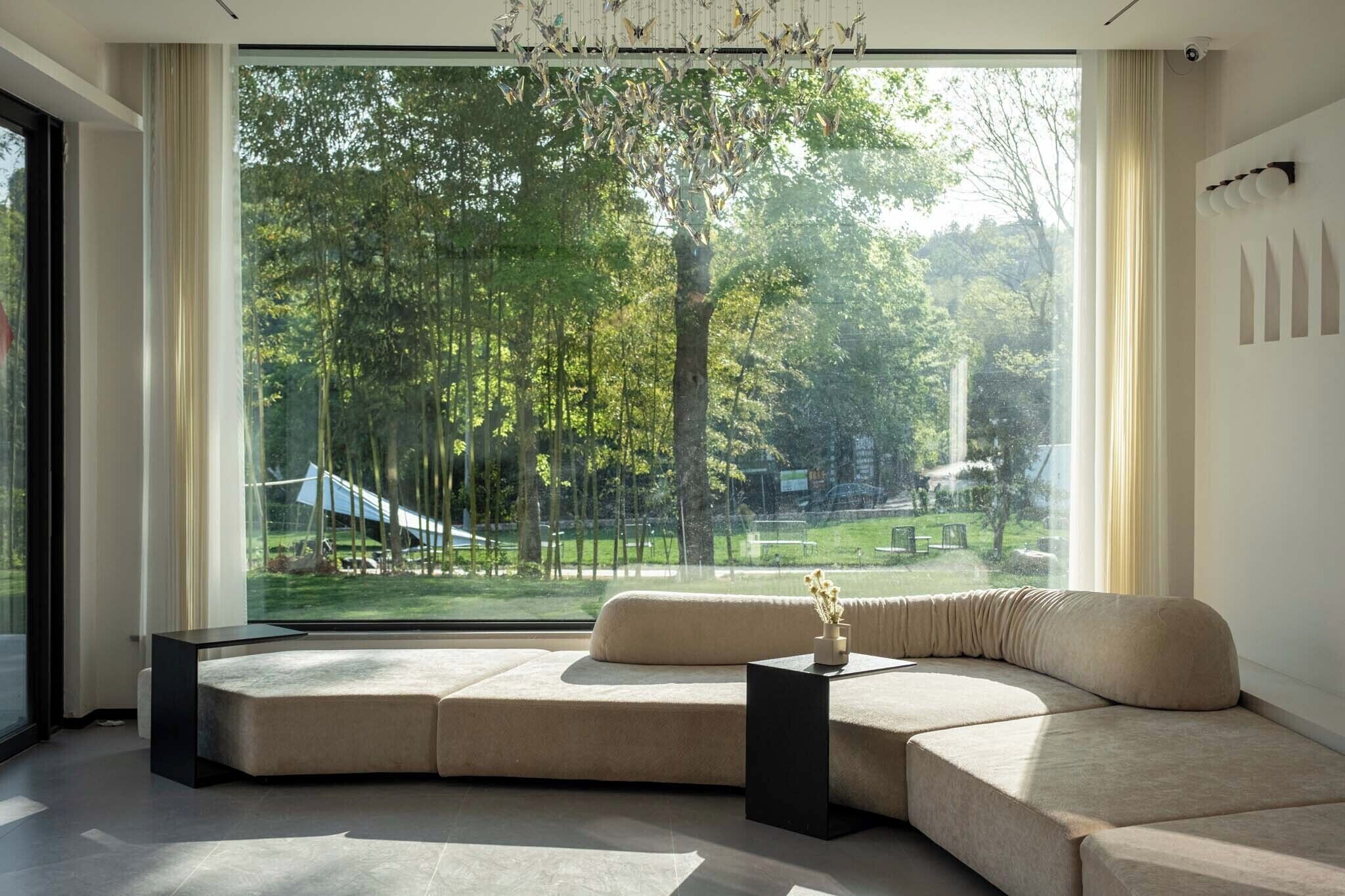 A modern living room with a large window, a sofa, a black side table, and a hanging light fixture.