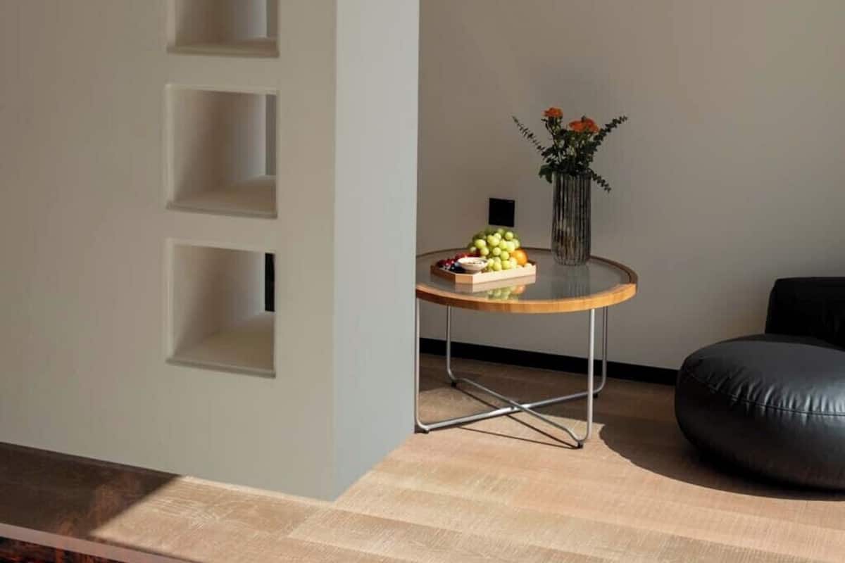 Un espace de vie moderne avec un mur incurvé, une table ronde agrémentée d’un vase et de fruits, et un fauteuil en cuir noir.