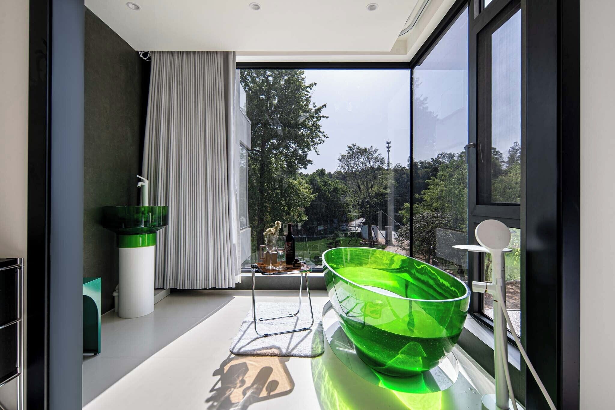 Un baño moderno con un ventanal grande, un cuenco de vidrio verde y un lavamanos blanco.