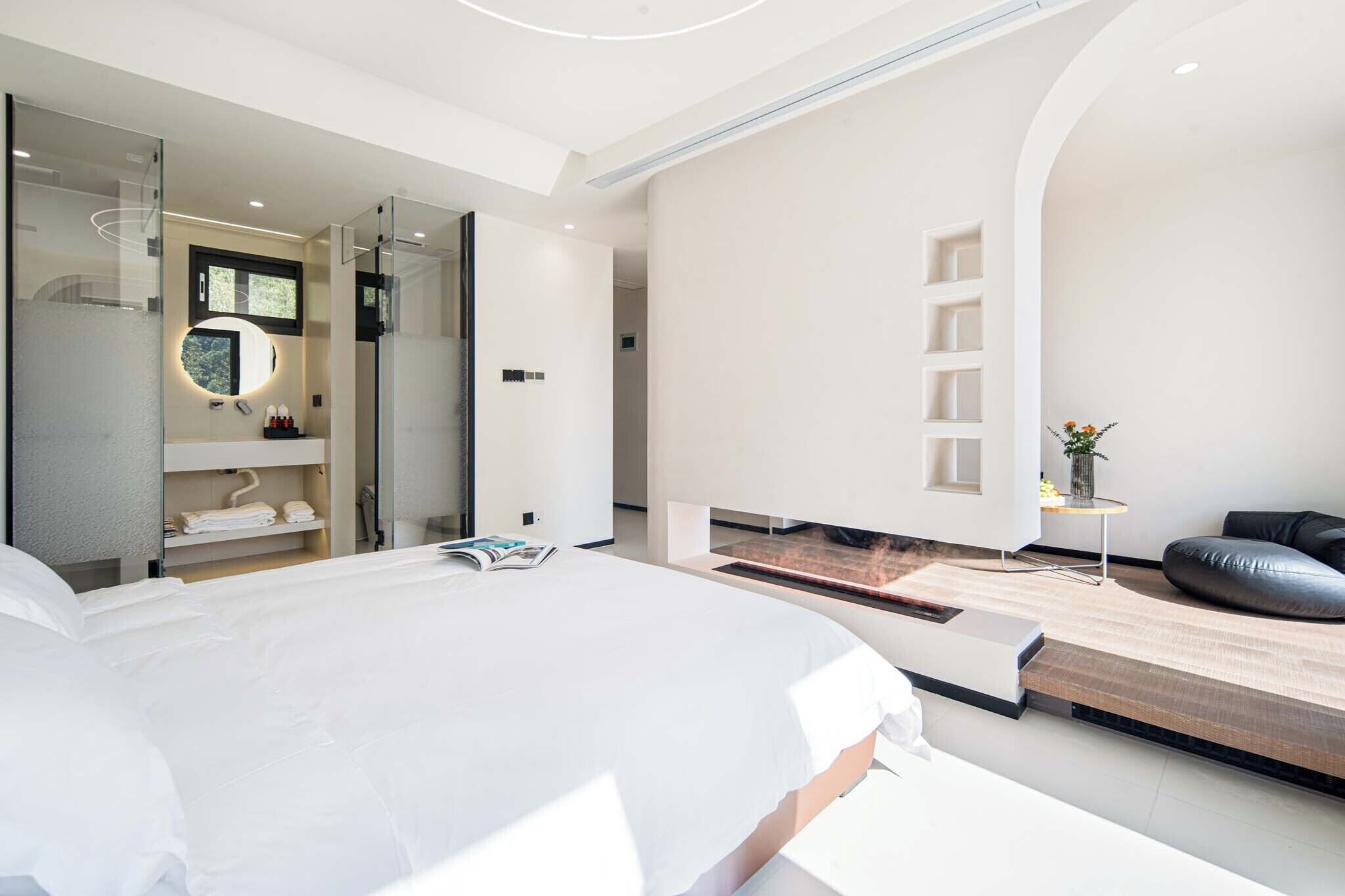 A modern bedroom with a large bed, a walk-in closet, and a small seating area with a view.