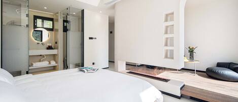 A modern bedroom with a large bed, a walk-in closet, and a small seating area with a view.