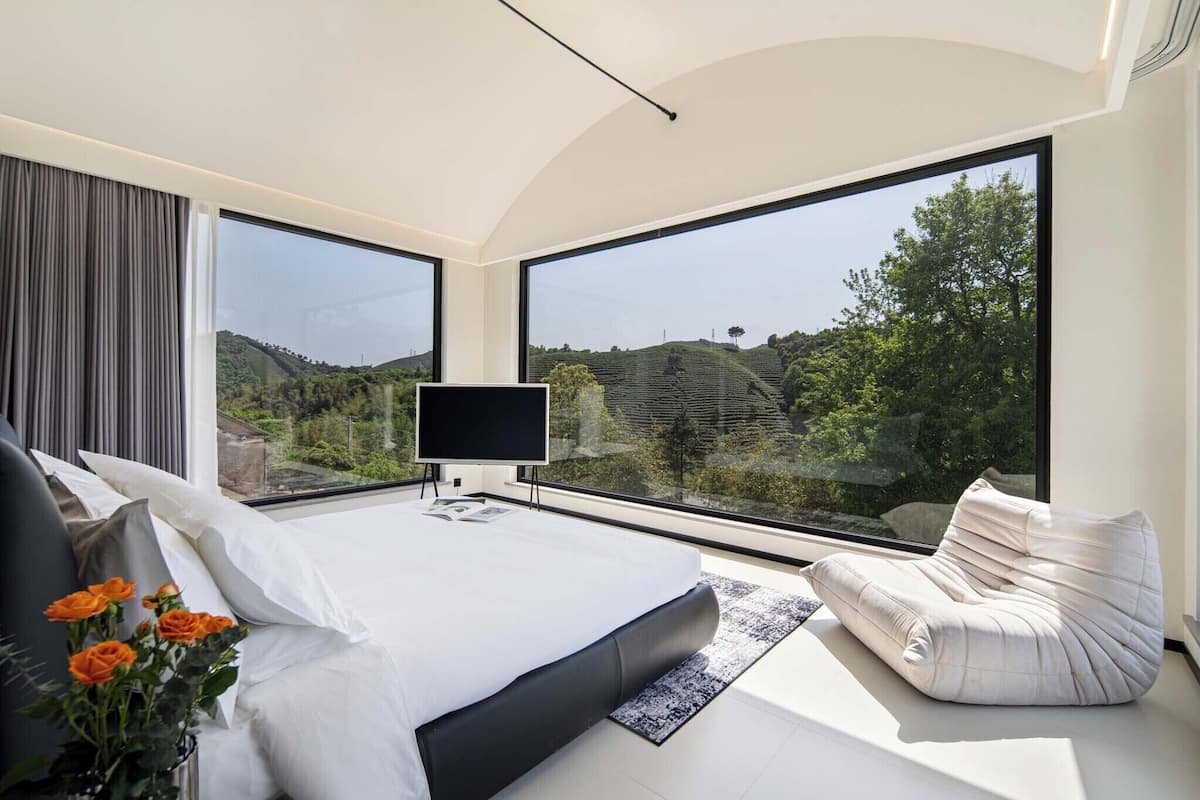 Une chambre moderne dotée d’un grand lit, d’un téléviseur à écran plat et offrant une vue sur un paysage vallonné grâce à de grandes fenêtres.
