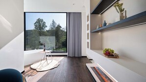 Ein modernes Zimmer mit großem Fenster, einem kleinen Tisch mit Stuhl, einem Regal mit Dekoration und einem Kamin.