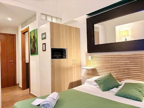 A hotel room with a bed, a wooden wardrobe, a built-in microwave, a mirror, and a bedside table. - Standard Double - InternoUno - Via Campaldino (Roma)
