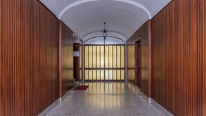 Um corredor com painéis de madeira, piso ladrilhado e vista através de uma porta de vidro.