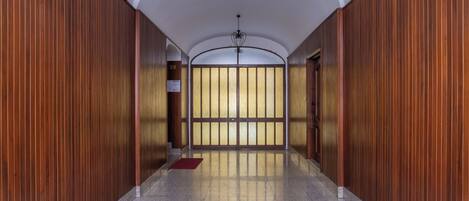 A hallway with wooden paneling, a tiled floor, and a view through a glass door.
