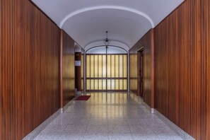 A hallway with wooden paneling, a tiled floor, and a view through a glass door.