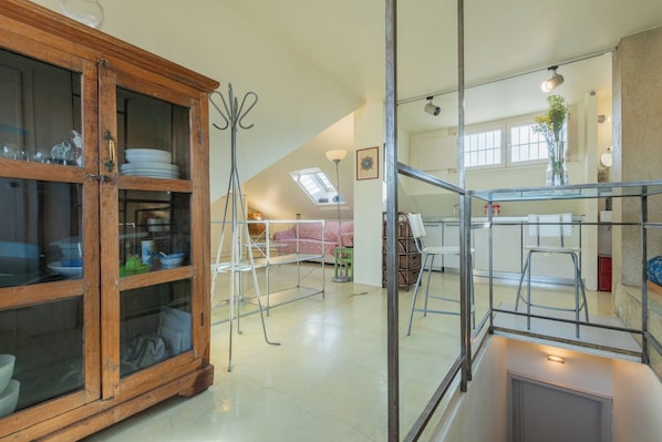 A spacious loft with a high ceiling, a wooden cabinet with glass doors, a metal ladder, and a skylight.