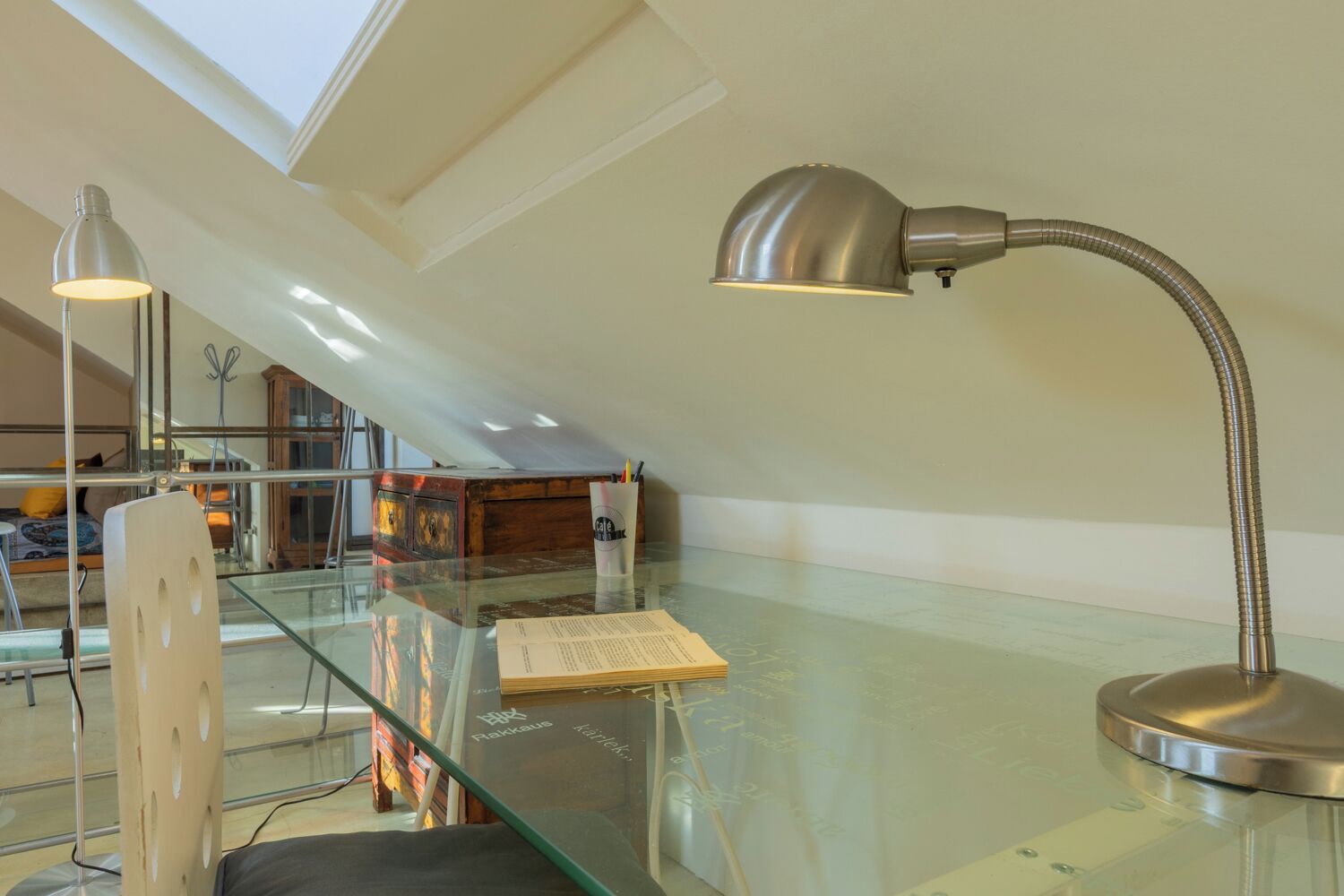 Un dormitorio estilo loft moderno con un escritorio de cristal, una lámpara de escritorio metálica y un tragaluz.