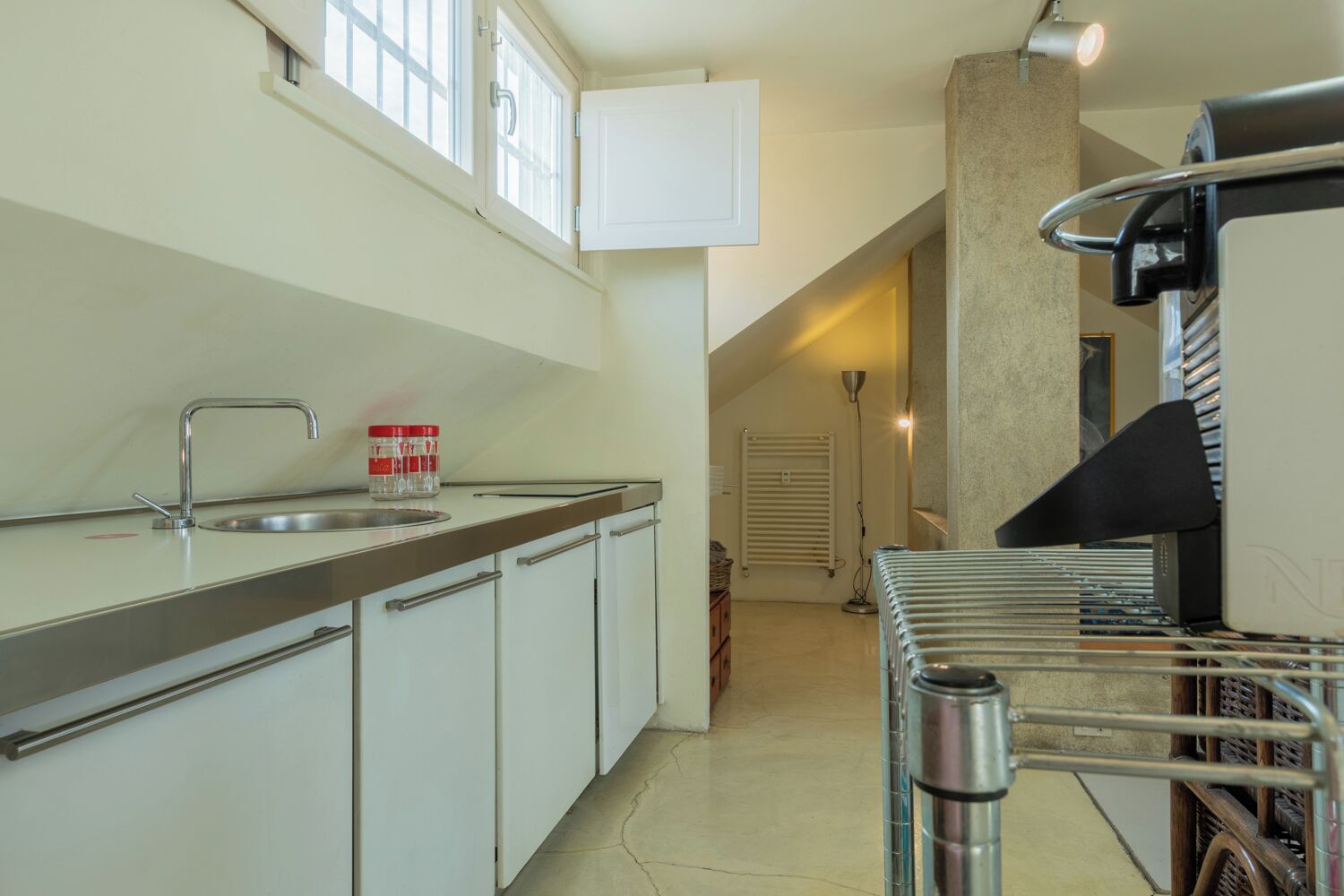 Une cuisine équipée d’un évier, de placards, d’une fenêtre et d’un radiateur.