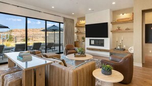 Uma sala de estar moderna com uma televisão grande, assentos confortáveis, uma lareira e vista para o deserto.