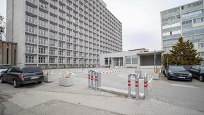 En modern byggnad med ett rutmönster av fönster, en grind vid ingången och parkerade bilar.