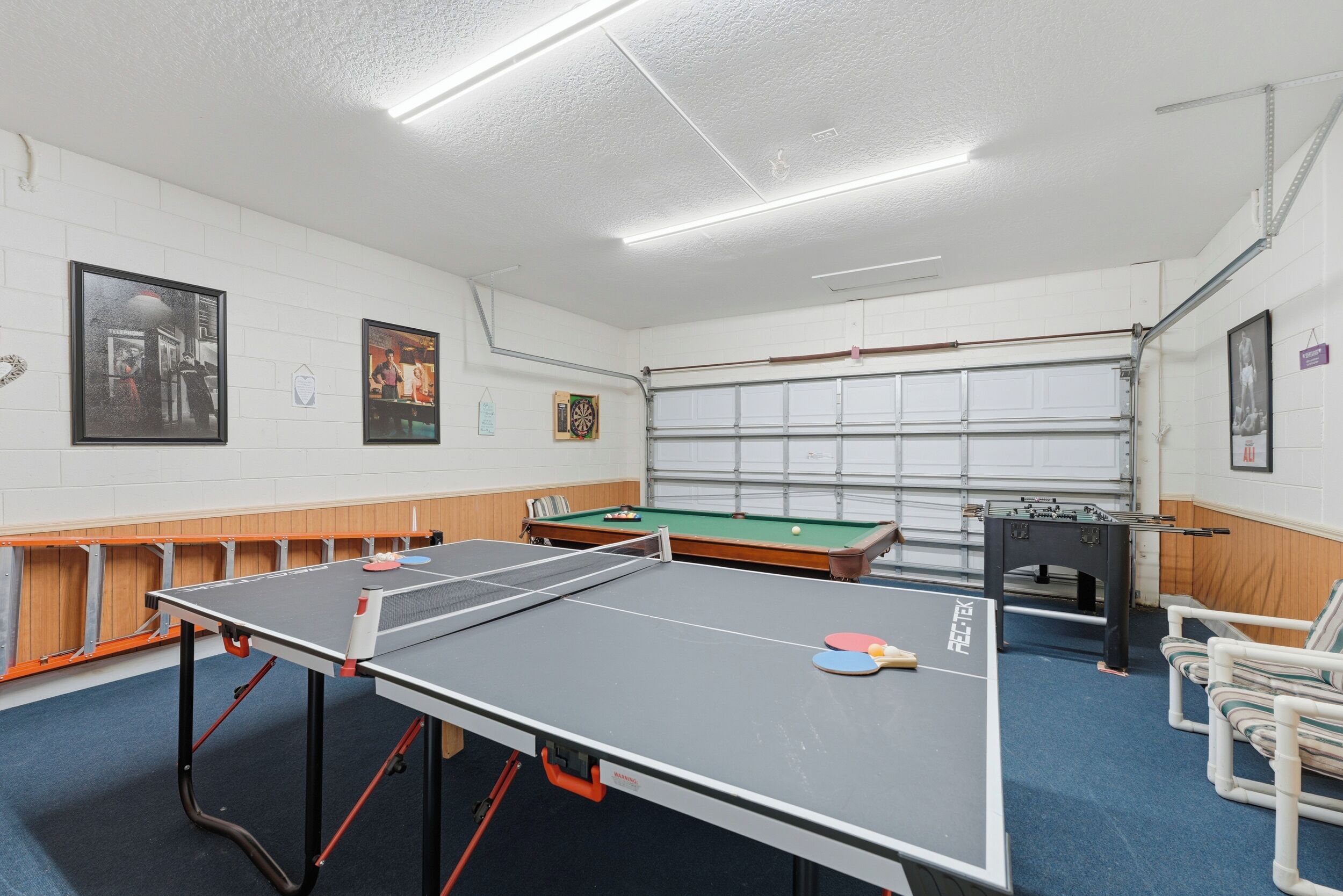 A room with a ping pong table, pool table, and foosball table.