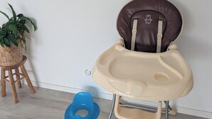Un seggiolone con seduta e schienale imbottiti, un vassoio e una gioietta blu sul pavimento.