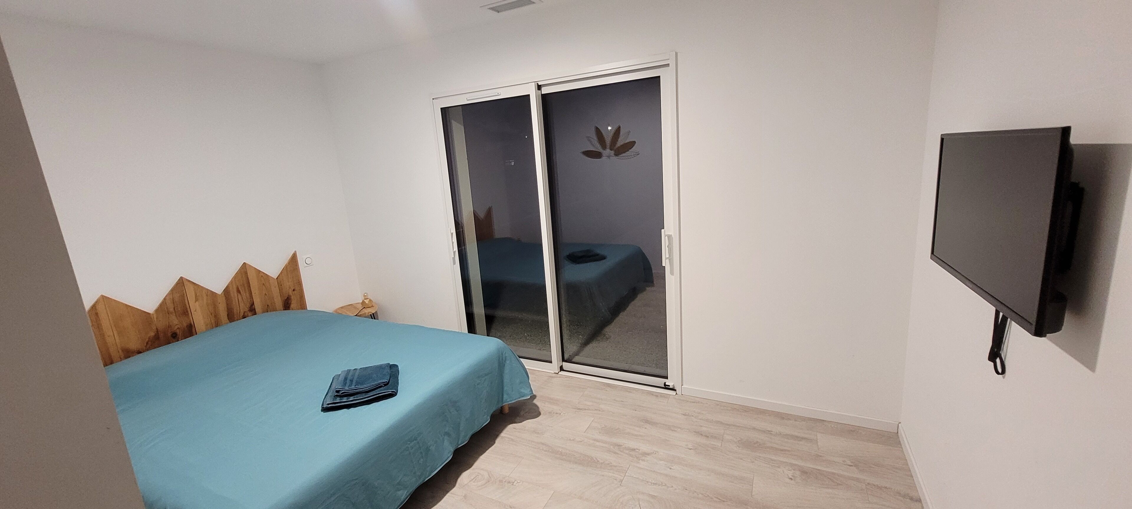 Un dormitorio con cama, puerta corrediza, televisor y cabecero de madera.