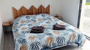 Un letto con copriletto a motivi fogliari, una testiera in legno, due comodini e vista sull'esterno.
