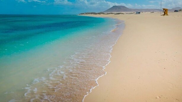 Une plage avec une eau turquoise et limpide, un rivage sablonneux et une tour de surveillance des sauveteurs.