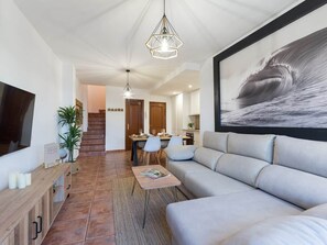 Ein modernes Wohnzimmer mit einer Couch, einem Couchtisch, einem Fernseher und einem Essbereich mit Stühlen und einem Tisch.