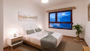 Quarto com cama, mesa de cabeceira, abajur, janela e vista do céu.