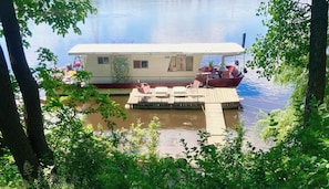 A houseboat docked at a pier with a small deck and seating area.