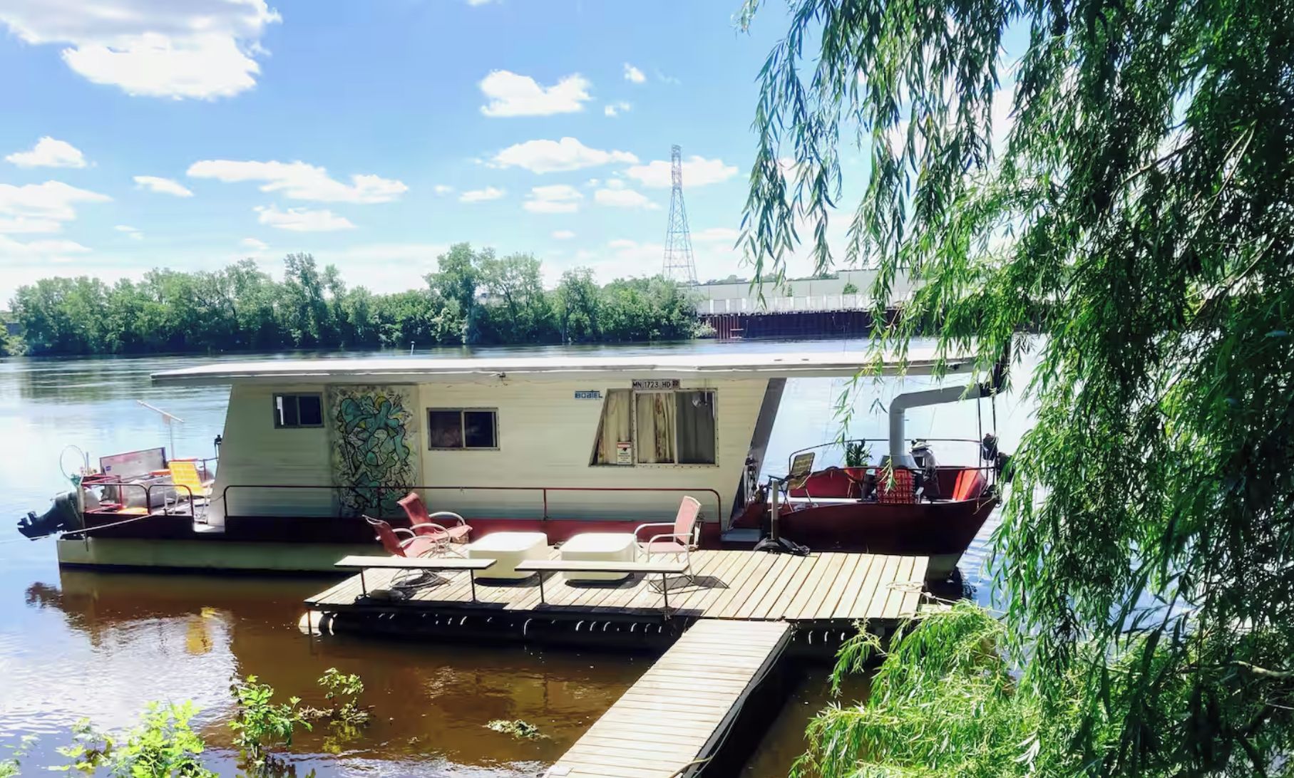 Una casa flotante amarrada en un muelle, con una pequeña terraza y un espacio de estar cubierto.