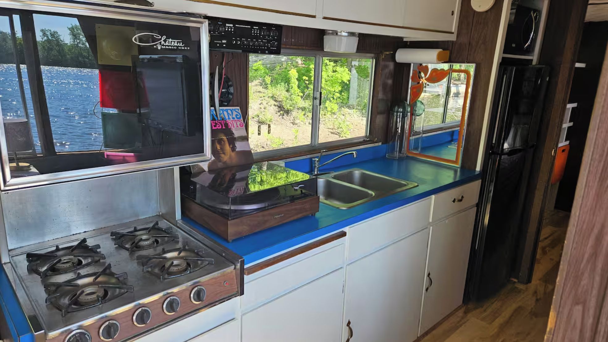 Een compacte keuken met een gasfornuis, een spoelbak en een raam met uitzicht op het water.
