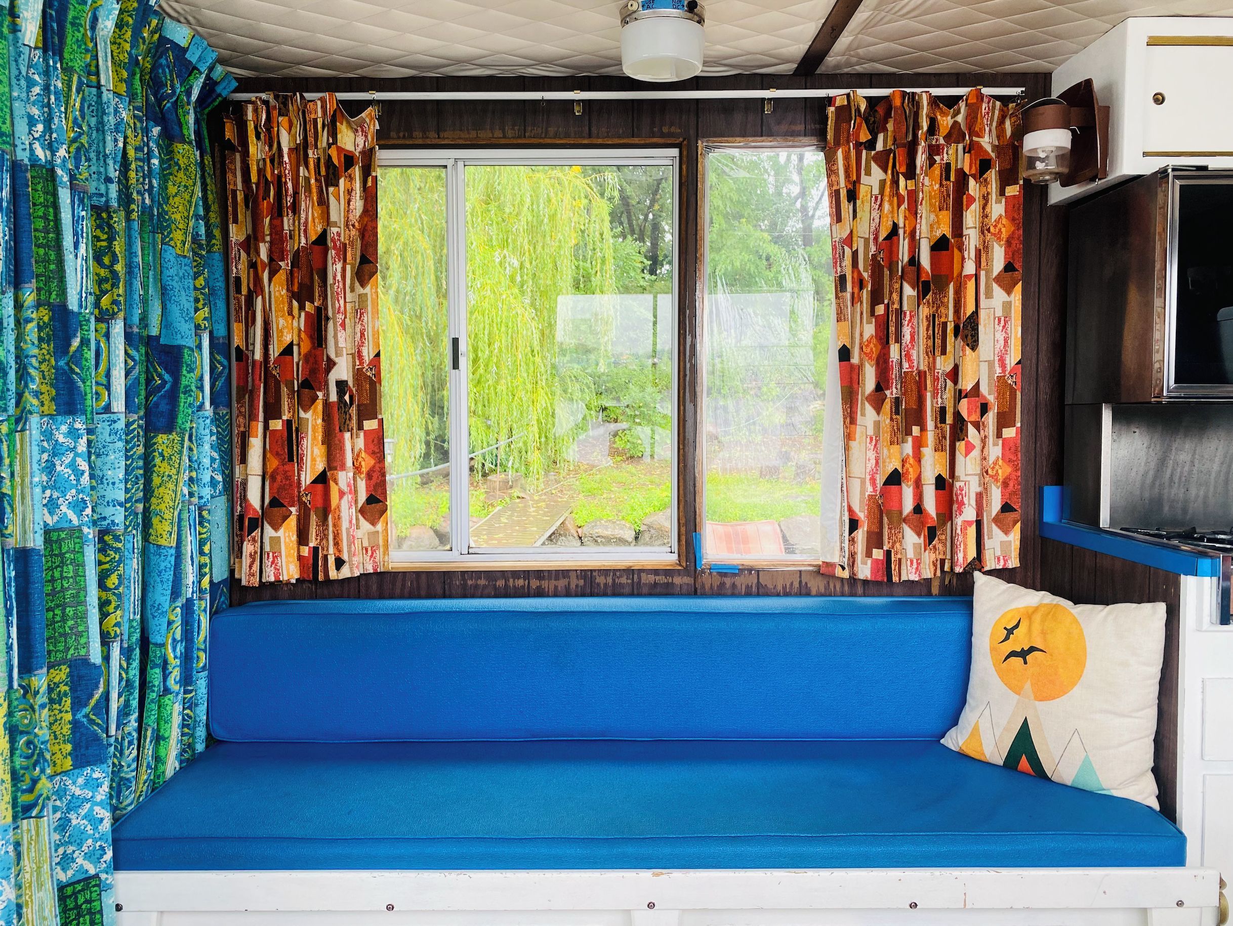A cozy interior with a blue bench, colorful curtains, and a view of greenery outside.