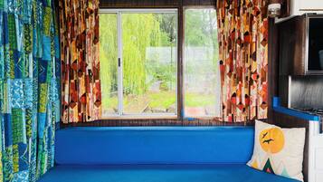 A cozy interior with a blue bench, colorful curtains, and a view of greenery outside.