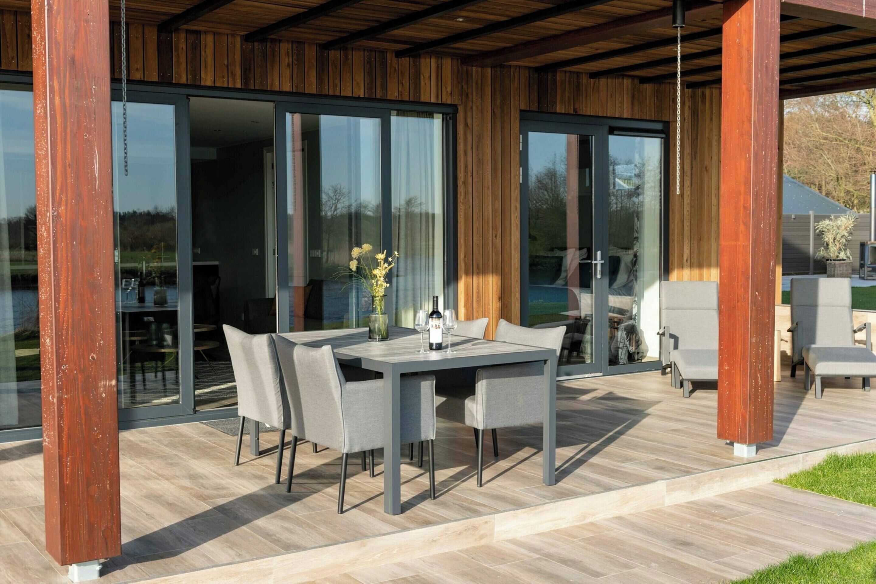 An outdoor patio with a dining table and chairs, a wooden pergola, and a glass door leading to an interior space.