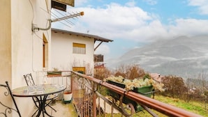 A balcony with a table and chairs, a white building, and a mountainous landscape in the background. - Ca' Fedon - Mountain View Terrace (Domegge di Cadore)
