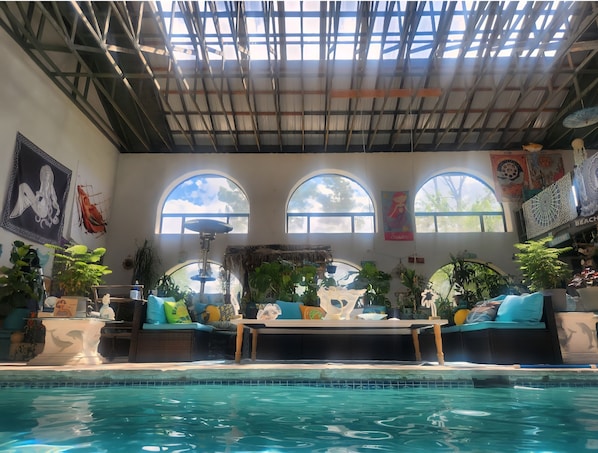 A poolside area with a clear view of the pool, a thatched roof, and various plants.