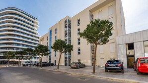 Un edificio moderno con fachada curva, coches aparcados y árboles a lo largo de la calle.