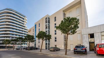 Un edificio moderno con fachada curva, coches aparcados y árboles a lo largo de la calle.