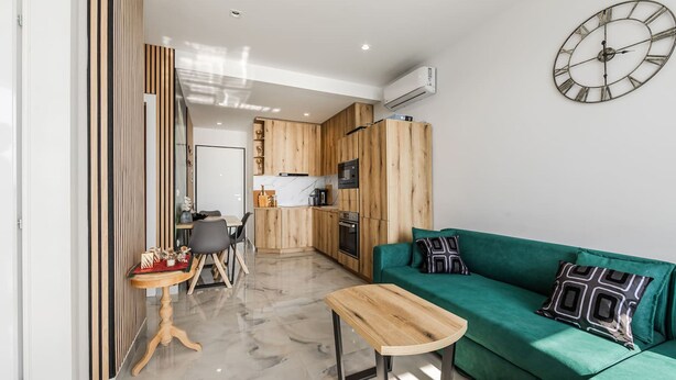 Una cocina moderna con armarios de madera, un sofá verde, una mesa de centro de madera y un reloj de pared.